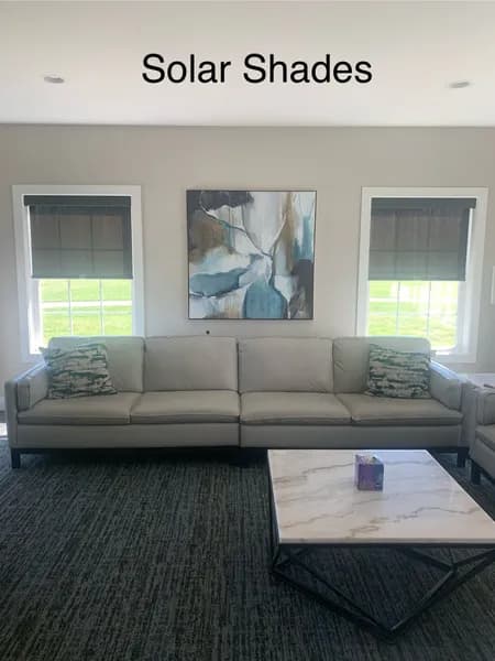 A living room with a couch, coffee table, and two windows with solar shades.